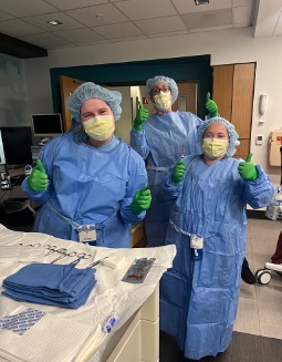three resdients in surgical gear give two thumbs up from an operating room